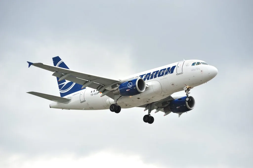 Aeronava TAROM în zbor, cu cer noros în fundal.