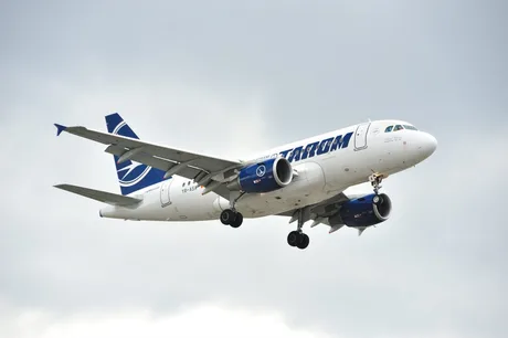 Aeronava TAROM în zbor, cu cer noros în fundal.