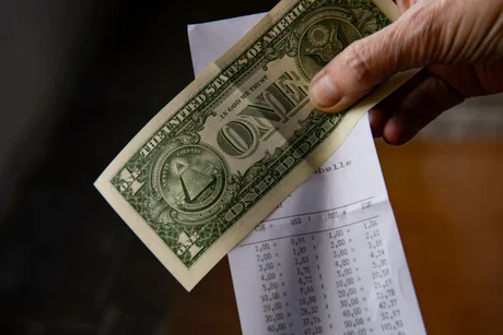 Un dolar american în mână, alături de un bon de plată.