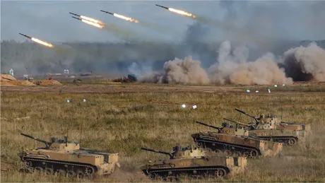 Exerciții militare cu tancuri și rachete în peisajul de câmp.