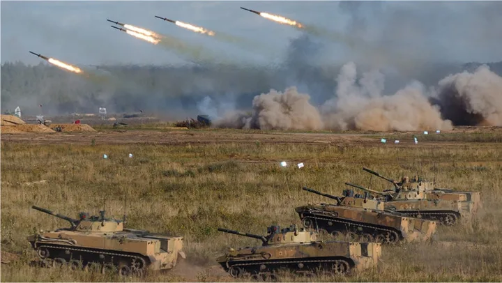 Exerciții militare cu tancuri și rachete în peisajul de câmp.