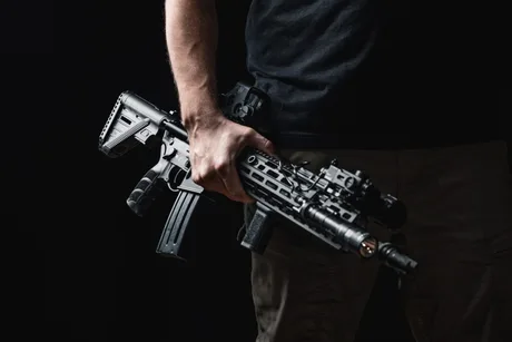 Un bărbat ține o pușcă de asalt în mână, pregătit pentru acțiune.