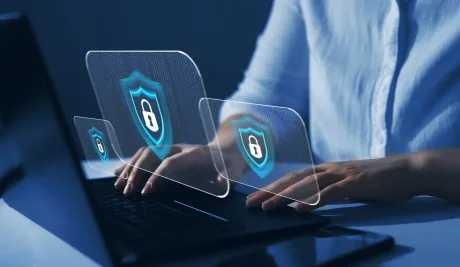 Persoană lucrând la un laptop cu simboluri de securitate cibernetică.
