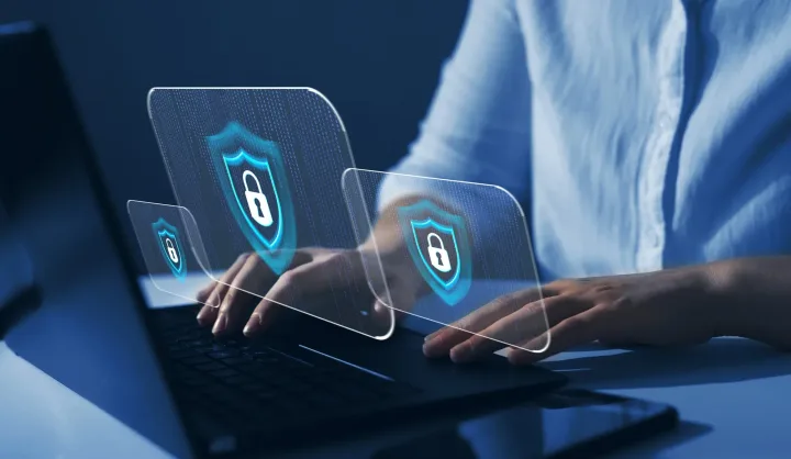 Persoană lucrând la un laptop cu simboluri de securitate cibernetică.