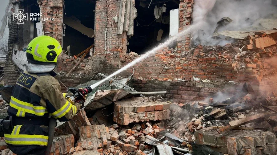 Pompier stingând flăcările într-o zonă afectată de bombardament.