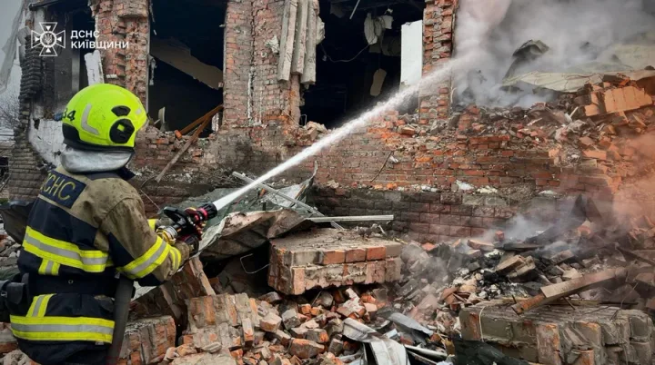 Pompier stingând flăcările într-o zonă afectată de bombardament.