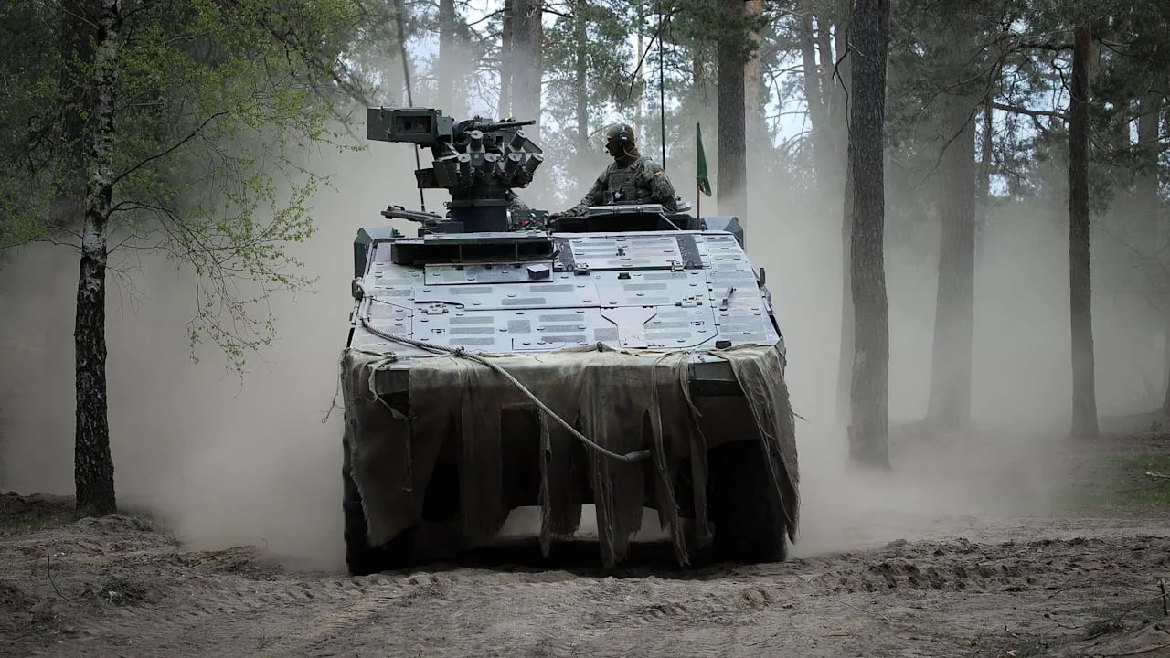 Tanc militar în mișcare printr-o pădure cu praf și vegetație.