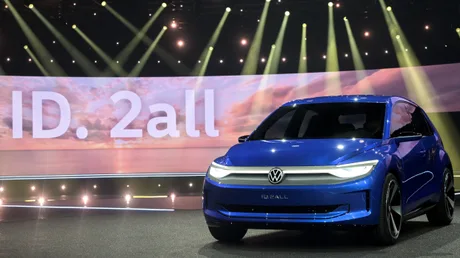 Volkswagen ID. 2all expus la un eveniment auto, cu lumini strălucitoare în fundal.