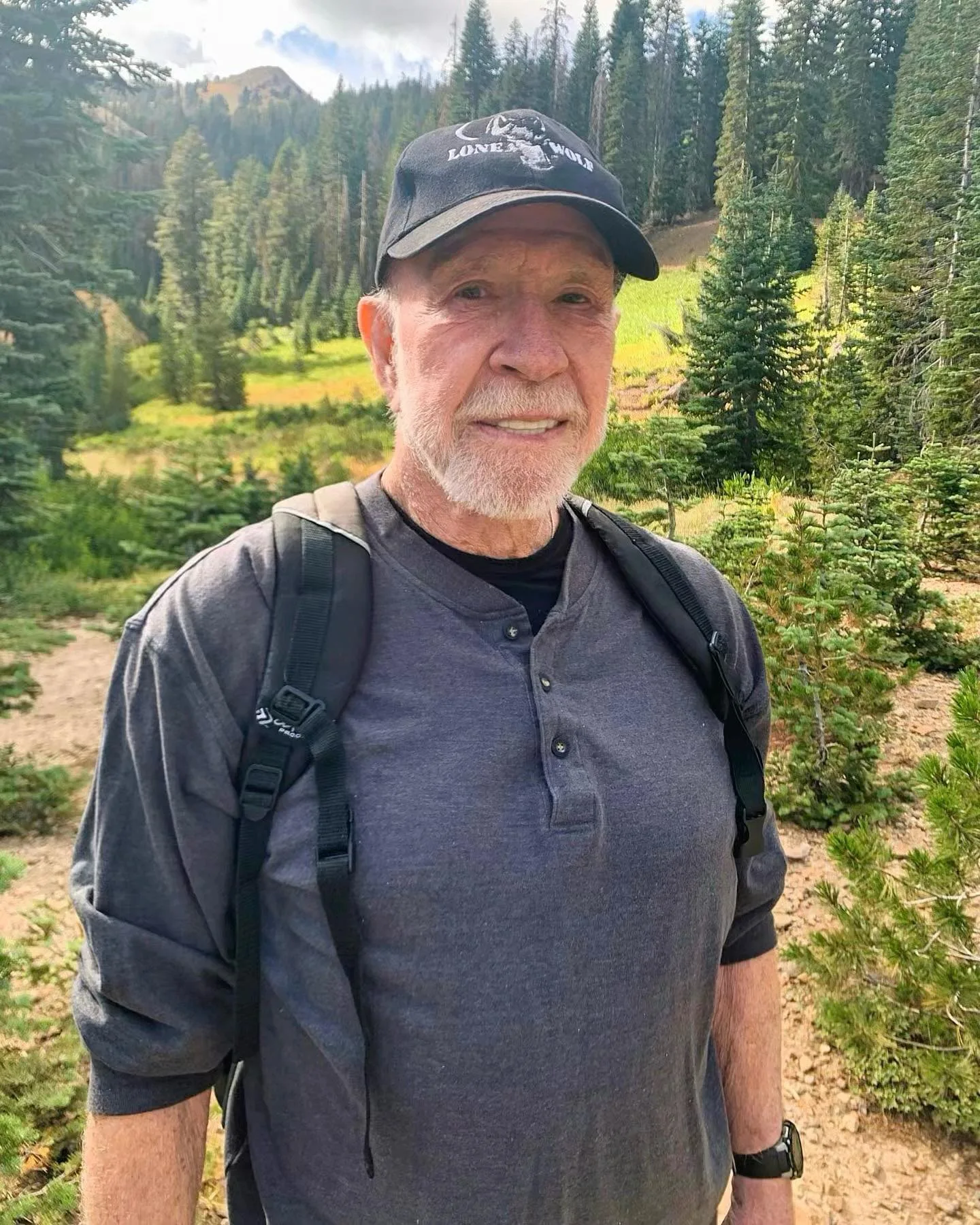 Chuck Norris zâmbind în natură, purtând o pălărie și rucsac.