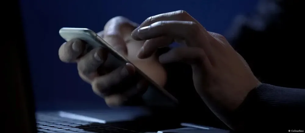 Mâini care folosesc un telefon mobil în întuneric, sugerând activități online.