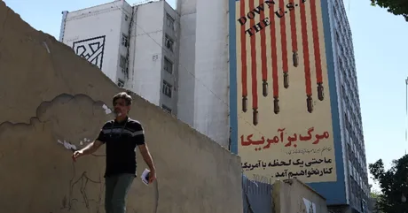 O persoană trece pe lângă un mural cu mesaje anti-americane în Iran.