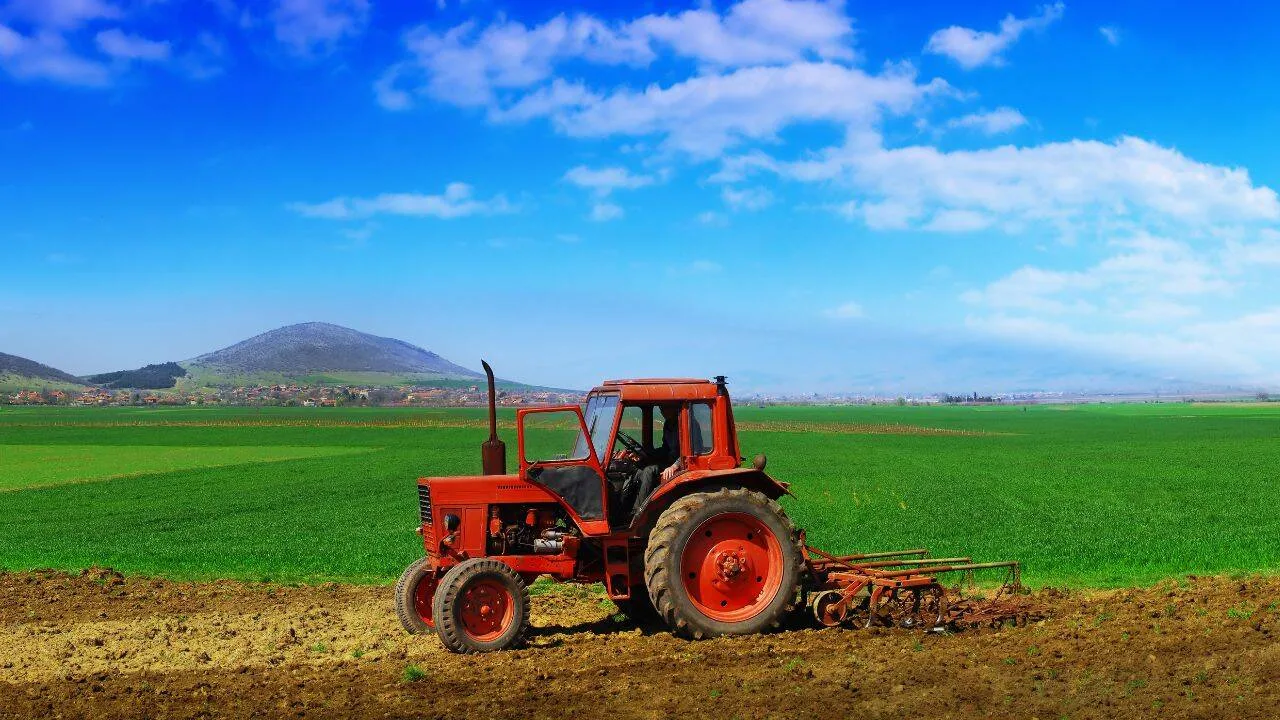 Tractor roșu pe câmp verde sub un cer senin.