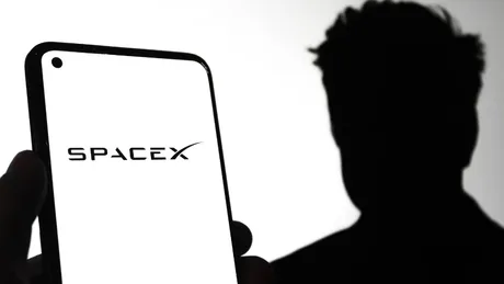 Logo-ul SpaceX pe un telefon, cu o siluetă în fundal.