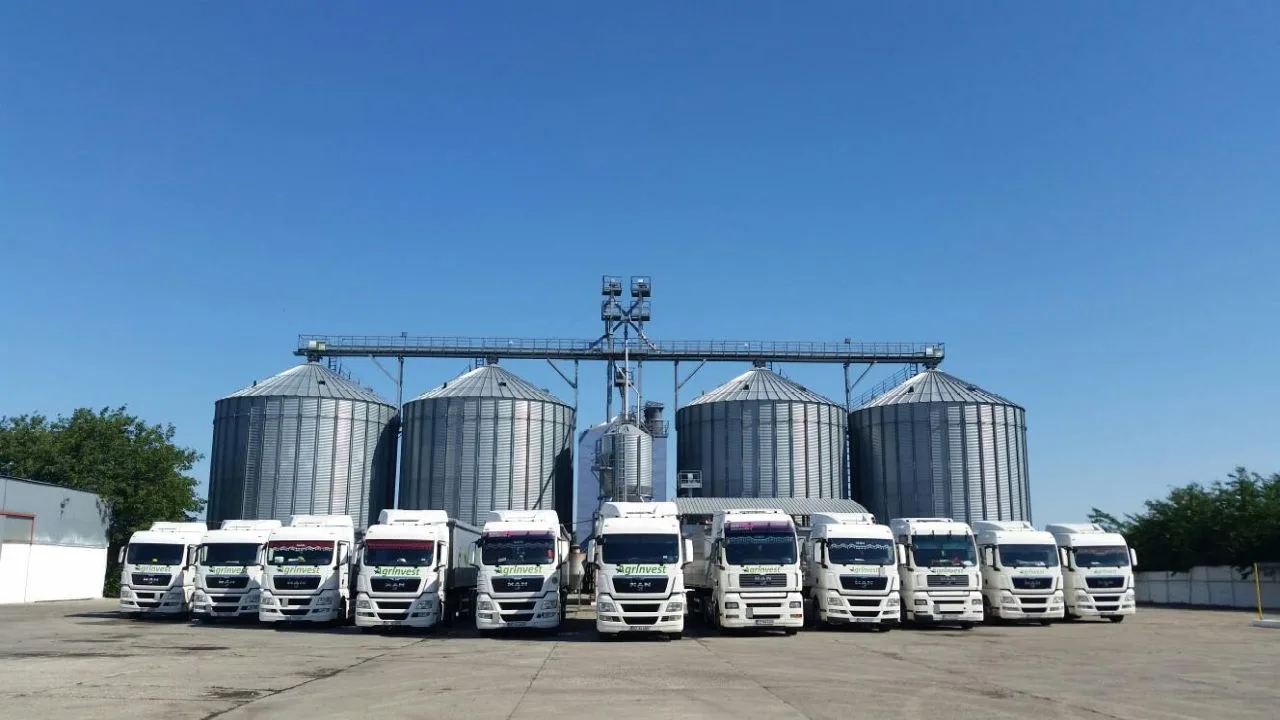 Flote de camioane parcate lângă silozuri de cereale sub un cer senin.