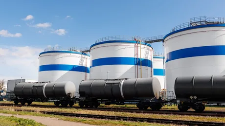 Rezervoare mari de substanțe chimice într-o zonă industrială, cu trenuri de marfă în apropiere.