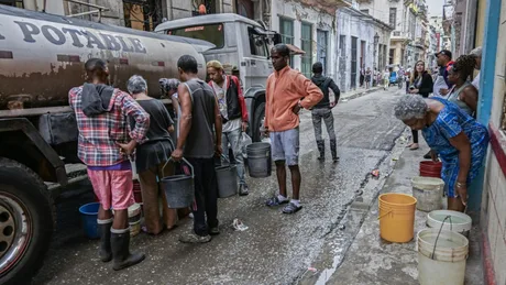 Oameni adunând apă potabilă pe o stradă din Havana.