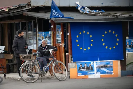 Bărbat și bătrân pe bicicletă lângă steagul Uniunii Europene.