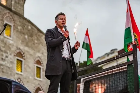 Peter Magyar vorbește la o conferință, cu steaguri în fundal.