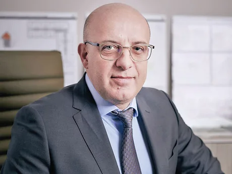 Un bărbat îmbrăcat la costum, cu o privire serioasă, stând în fața unui birou.