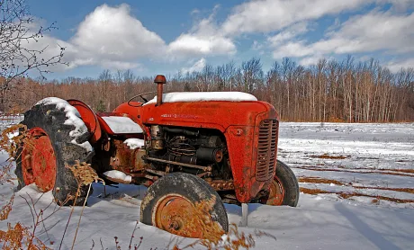 Tractor vechi acoperit cu zăpadă într-un peisaj agricol.