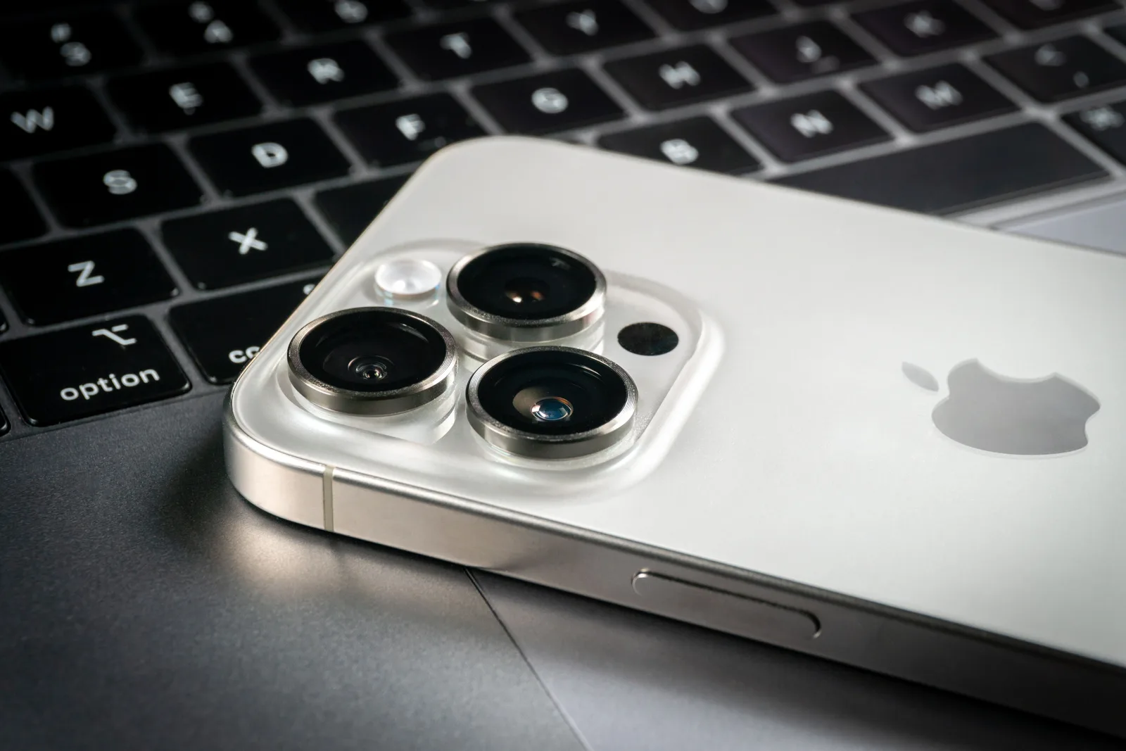 Detaliu al camerei unui smartphone Apple pe un fundal de laptop.