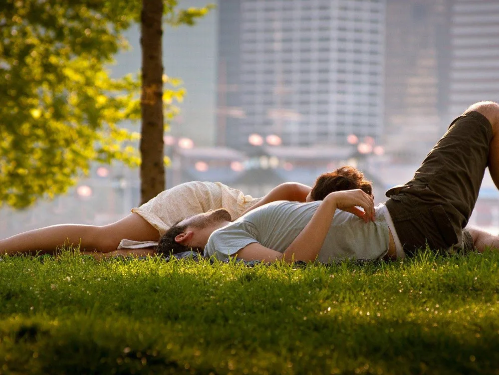 Tineri relaxându-se pe iarbă într-un parc, bucurându-se de vremea frumoasă.