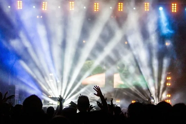 Aglomerație la concert, lumini strălucitoare și public entuziast.