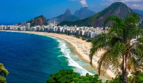 Plaja Copacabana din Rio de Janeiro, cu palmieri și clădiri pe fundal.
