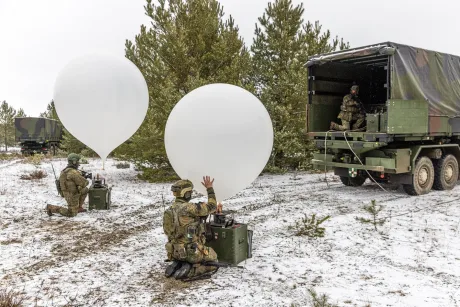 Soldați pregătesc baloane în pădure, în condiții de iarnă.