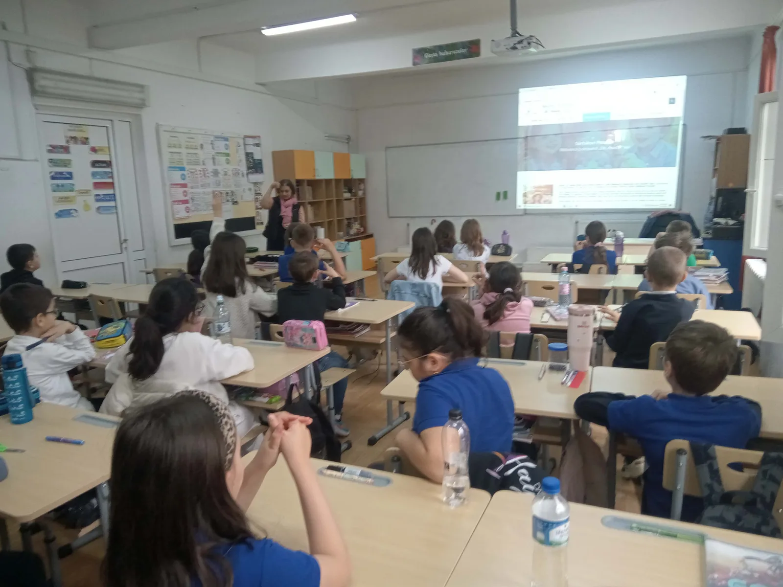 Elevi într-o clasă, ascultând o prezentare despre educație și finanțare.