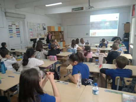 Elevi într-o clasă, ascultând o prezentare despre educație și finanțare.