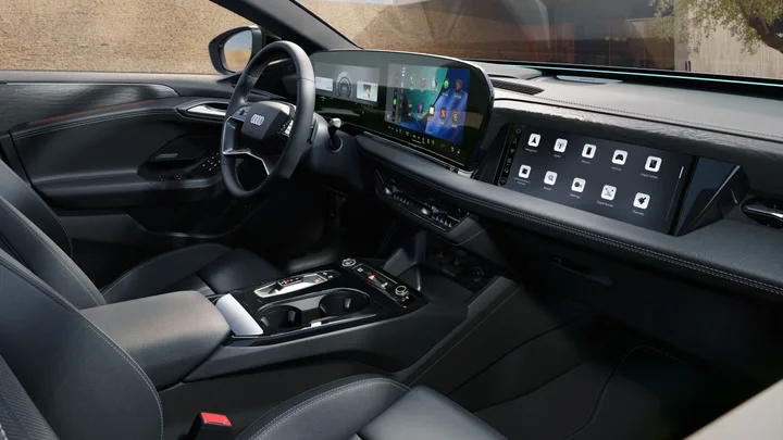 Interior modern al unui automobil Audi, cu ecrane digitale și butoane fizice pe volan.