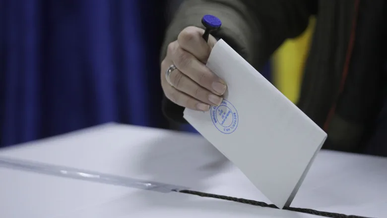 O mână introduce un buletin de vot într-o urnă electorală.