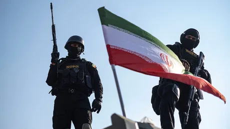 Doi soldați în uniformă, lângă steagul Iranului, într-un context de tensiune politică.