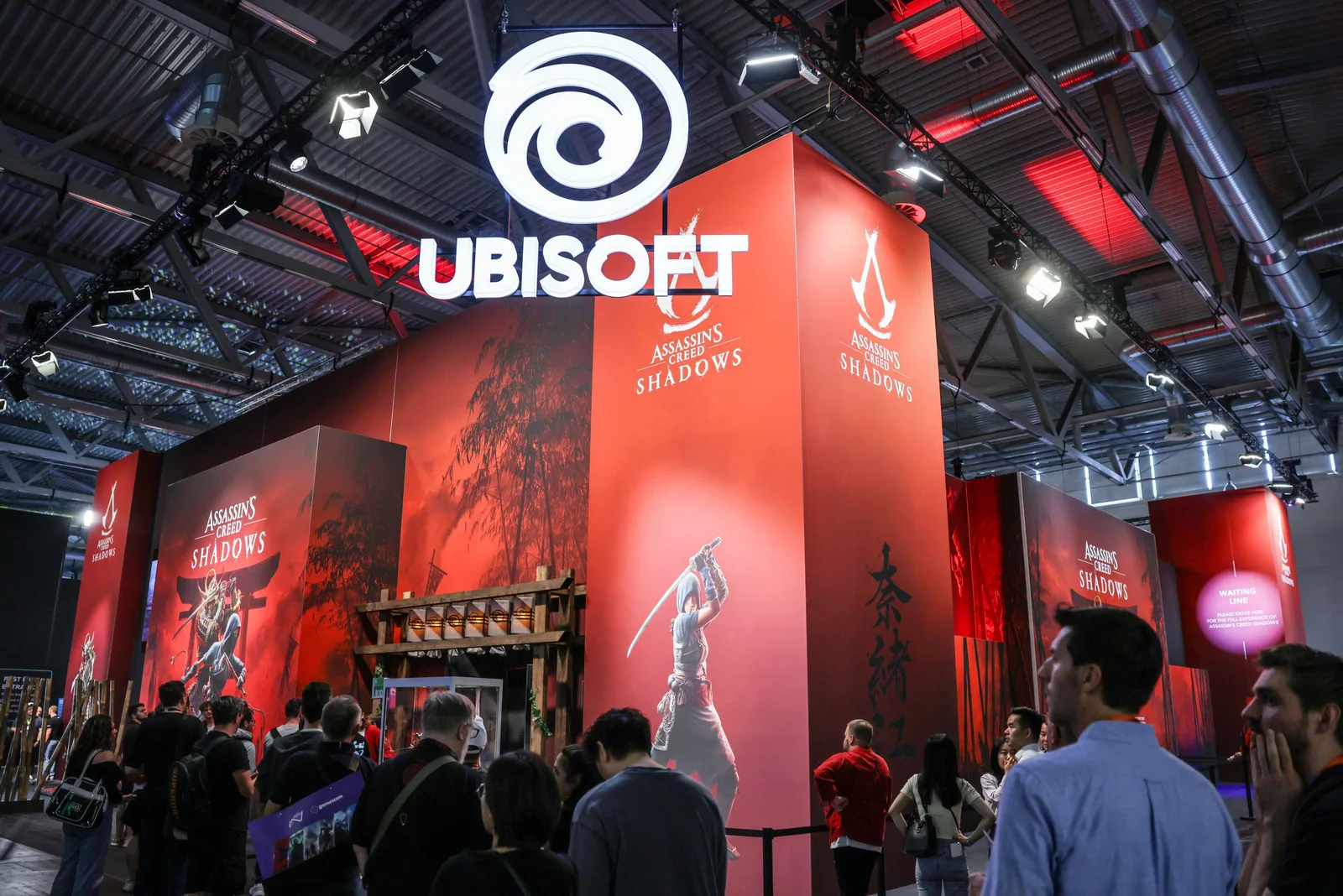 Stand Ubisoft la un eveniment, cu oameni admirând produsele și grafica.