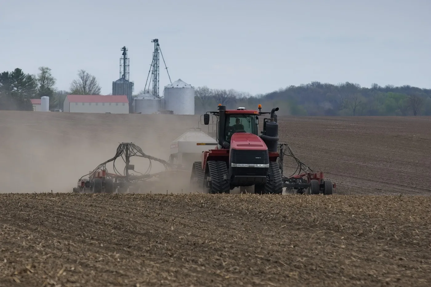 Tractor lucrând pe un câmp agricol, în condiții de praf și vânt.