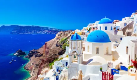 Peisaj idilic din Santorini, cu case albe și cupole albastre, lângă mare.