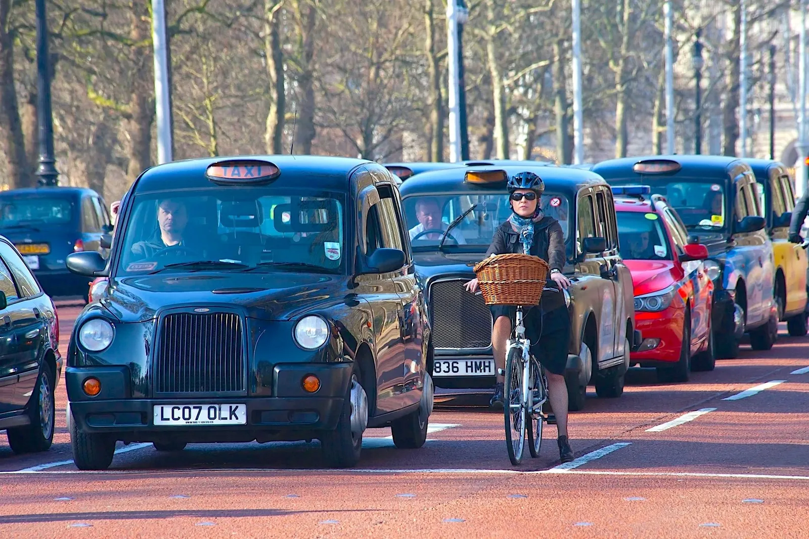 Ciclist pe stradă, înconjurat de taxiuri londoneze pe o zi însorită.