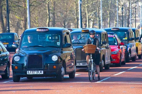 Ciclist pe stradă, înconjurat de taxiuri londoneze pe o zi însorită.