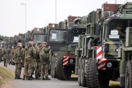 Militari germani discutând lângă vehicule militare pregătite pentru desfășurare.