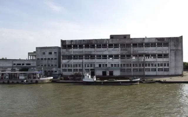 Clădire abandonată pe malul unui râu din România, simbol al industriei neutilizate.