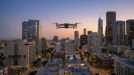 Dronă zburând deasupra unui oraș modern la apus.