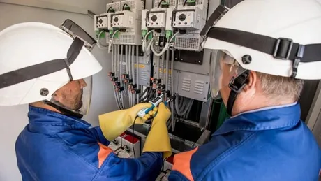 Tehnicieni inspectând echipamente electrice într-o stație de energie.