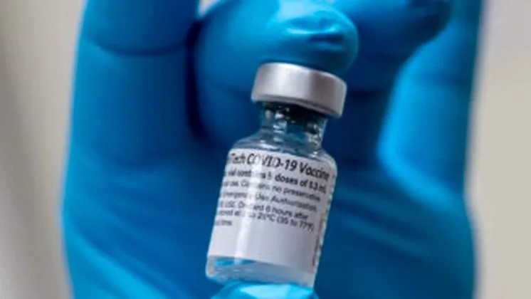 Flacon de vaccin COVID-19 ținut de o mână acoperită cu mănușă.