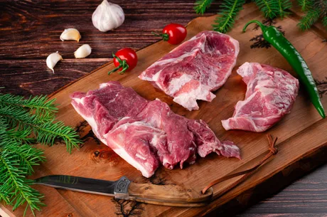 Carne de miel proaspătă pe un fundal de lemn, alături de condimente.