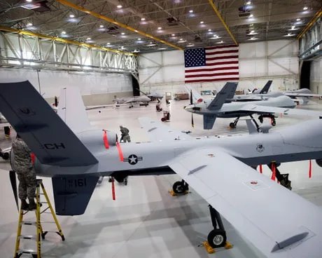 Drone militare pregătite într-un hangar cu steagul american.