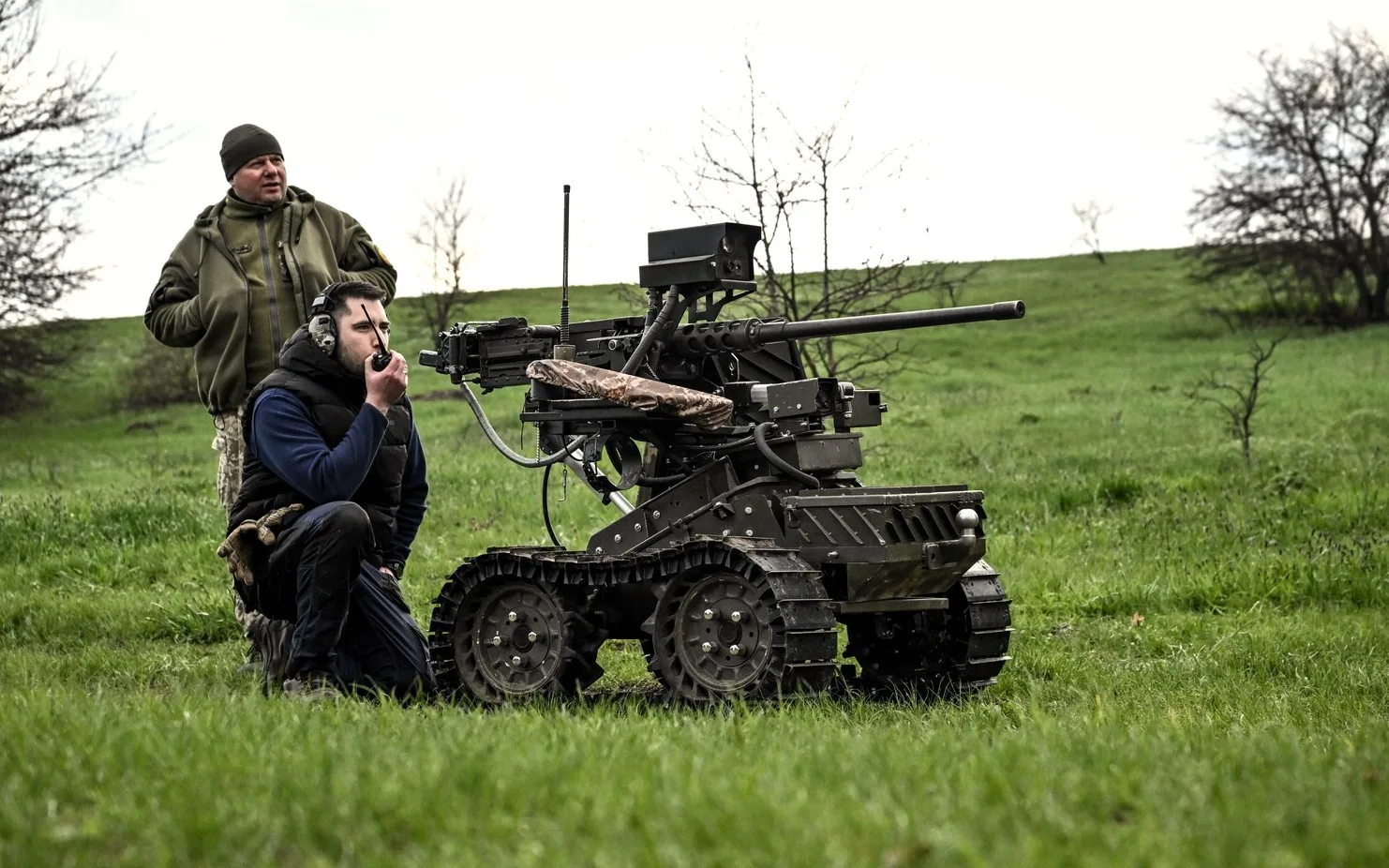 Doi soldați operând un robot militar pe un câmp verde.
