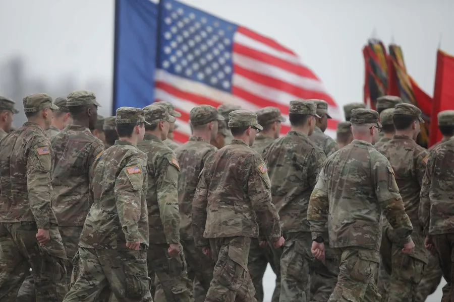Soldați americani în timpul unei parade militare, cu steagul SUA în fundal.