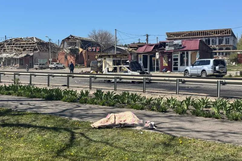 Peisaj urban afectat de conflict, cu clădiri deteriorate și vegetație înfloritoare.
