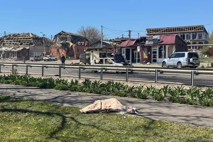 Peisaj urban afectat de conflict, cu clădiri deteriorate și vegetație înfloritoare.